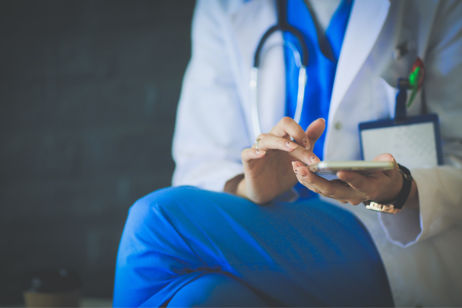 A doctor, clad in medical attire with a stethoscope draped around their neck, diligently uses a smartphone, possibly accessing the latest Covid-19 study through Sermo.