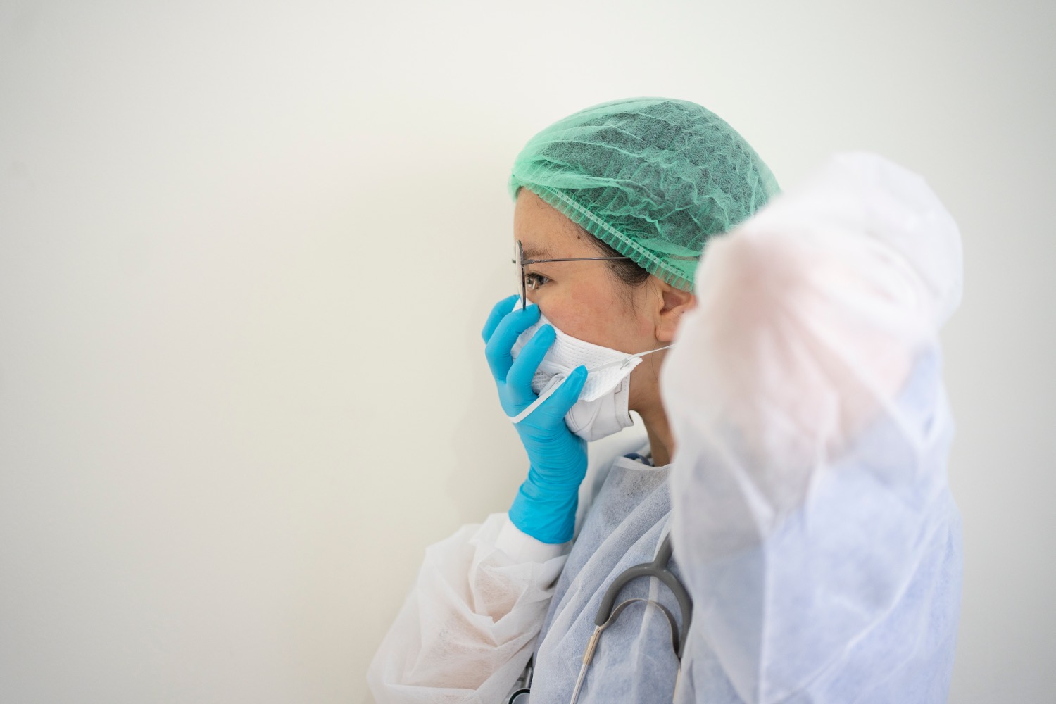 A dedicated healthcare worker in scrubs, gloves, and a green hairnet adjusts a face mask, embodying the essential role during the COVID-19 pandemic.