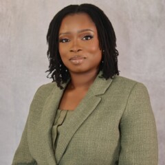 A woman with medium-length locs, identified as Abimbola Ekundayo, MD, wears a green blazer as she poses for a formal portrait against a light gray background.