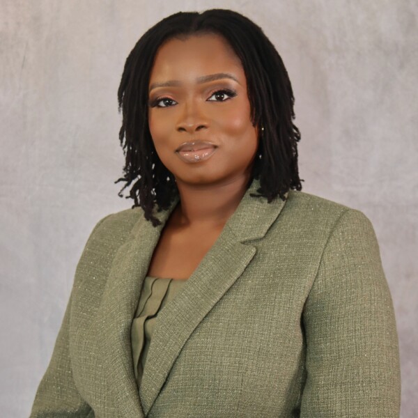 A woman with medium-length locs, identified as Abimbola Ekundayo, MD, wears a green blazer as she poses for a formal portrait against a light gray background.
