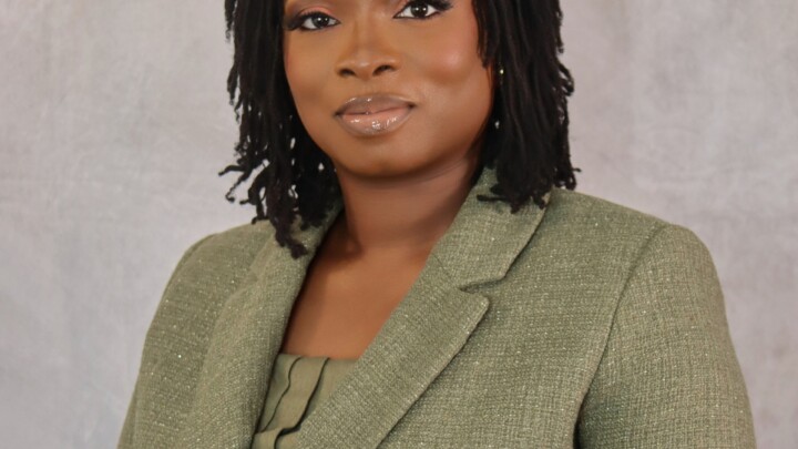 A woman with medium-length locs, identified as Abimbola Ekundayo, MD, wears a green blazer as she poses for a formal portrait against a light gray background.