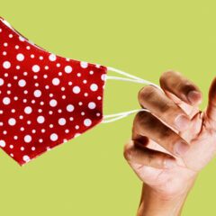 red and white dotted face mask held by a hand against a light green background