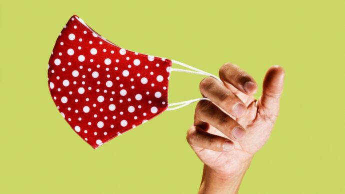 red and white dotted face mask held by a hand against a light green background