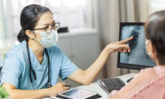female doctor wearing face mask educating patient of x-ray on screen