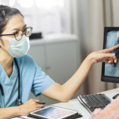 female doctor wearing face mask educating patient of x-ray on screen