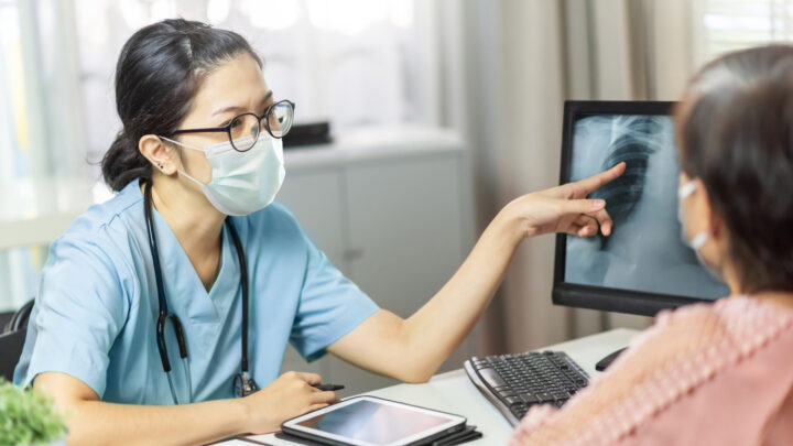 female doctor wearing face mask educating patient of x-ray on screen