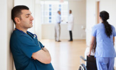 doctor leaning against a wall in a hospital hallway, eyes closed, arms crossed