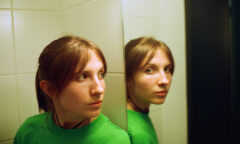 woman in green looking at a mirror that's looking at the camera