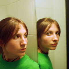 woman in green looking at a mirror that's looking at the camera