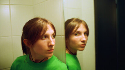 woman in green looking at a mirror that's looking at the camera