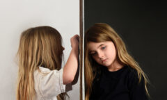 Young girl in white coloring on wall next to young girl in black looking sad