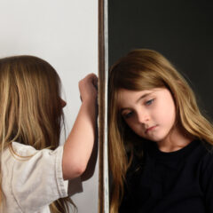 Young girl in white coloring on wall next to young girl in black looking sad