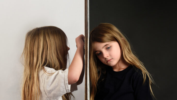 Young girl in white coloring on wall next to young girl in black looking sad