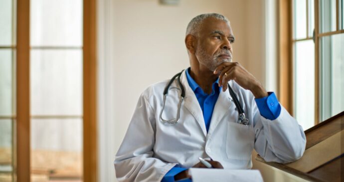 A doctor in a white coat with a stethoscope looks thoughtfully out the window, contemplating how to start a medical practice, while holding a clipboard.