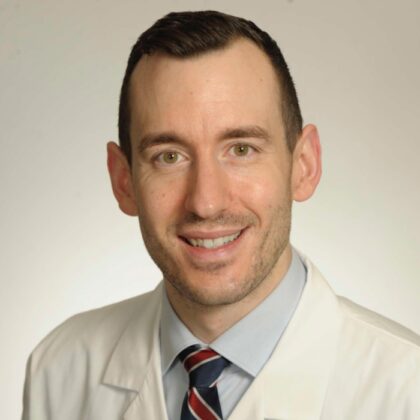 Patrick Fleming, MD, in a crisp white coat and tie, smiles warmly at the camera against a plain background.