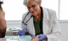 A doctor in a white coat and purple gloves conducts a finger-prick test on a patient, utilizing a small lancet device to ensure accurate results in line with CDC HIV guidelines.