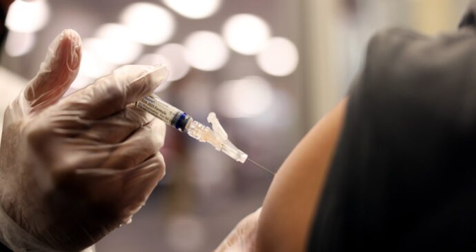 A healthcare worker administers a vaccine injection into a person's arm.