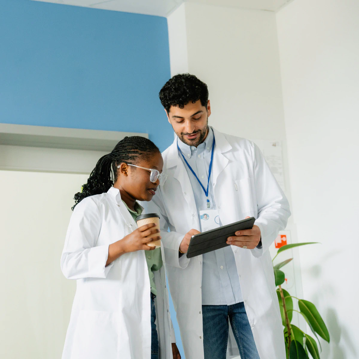 Two medical professionals in white coats discuss on a tablet.