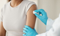 A healthcare provider wearing blue gloves cleans a woman's upper arm with a cotton ball in preparation for an injection, following the latest recommendations and ACIP guidelines.