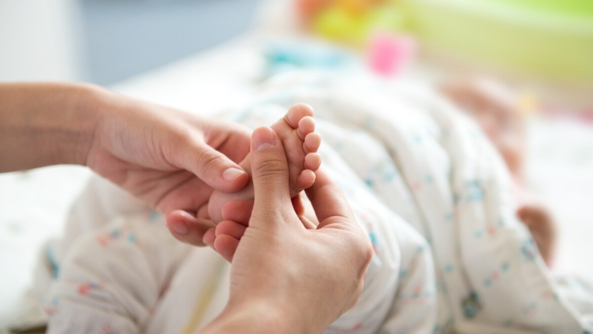 Close-up of an adult gently massaging a baby's foot while the baby lies wrapped in a blanket, highlighting a soothing moment trusted by top baby brands.