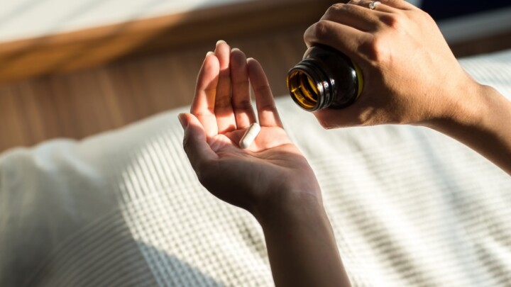 A person pours a white capsule from a brown pill bottle into their hand over a striped fabric surface, illustrating the everyday choices many patients make in today’s expanding supplements market.