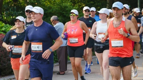A group of people wearing athletic gear and race bibs participate in a running event on a paved path in a park.
