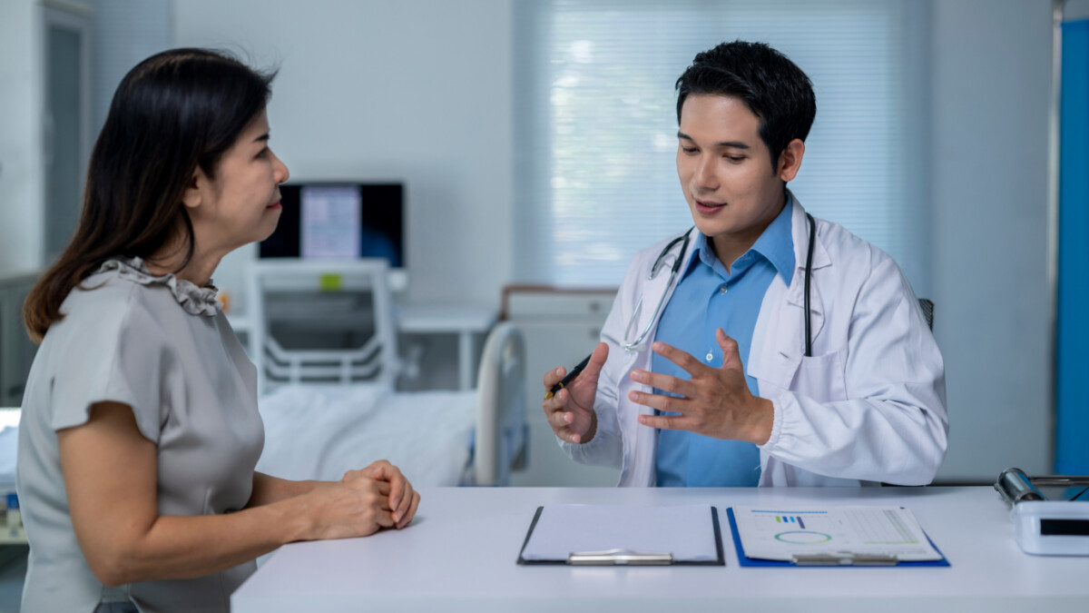 A doctor in a white coat—one of the many skilled physicians—explains the risk of Hantavirus to a seated patient across a desk with documents in a medical office.