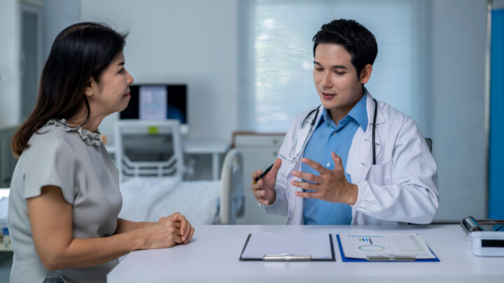 A doctor in a white coat—one of the many skilled physicians—explains the risk of Hantavirus to a seated patient across a desk with documents in a medical office.