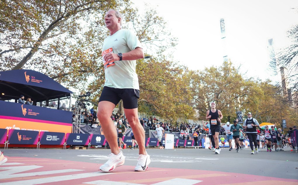 A group of runners cross a race finish line outdoors, with spectators and trees in the background on a clear day, celebrating that life is worth running.