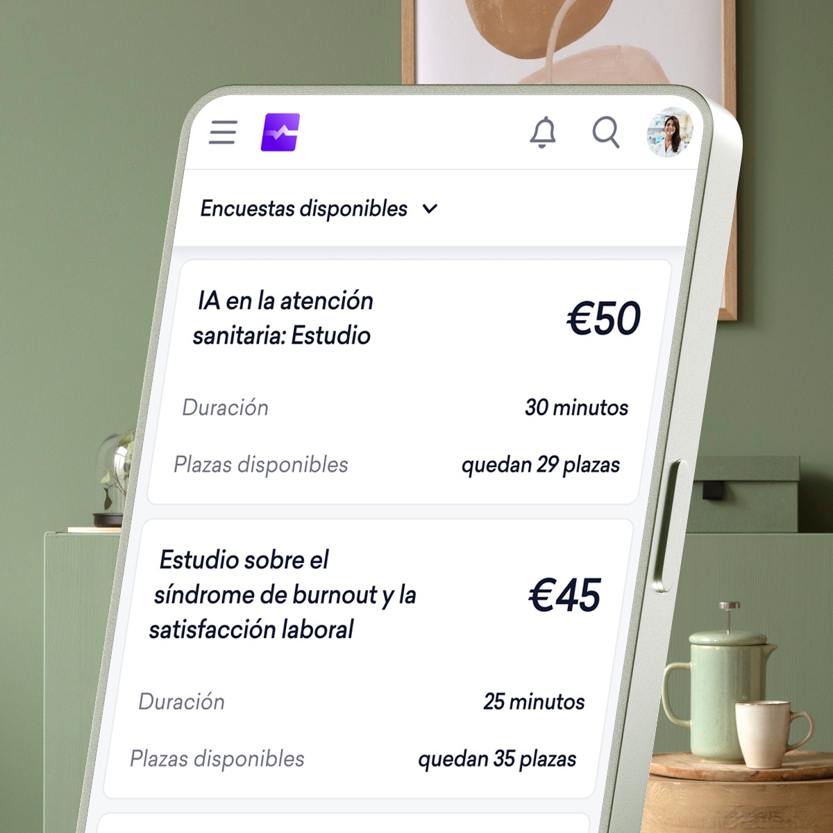Pantalla de un smartphone en la que se muestra una aplicación de encuestas con dos estudios disponibles: uno sobre la inteligencia artificial en el ámbito sanitario dirigido a dermatólogos (recompensa de 50 €) y otro sobre el agotamiento laboral y la satisfacción laboral (recompensa de 45 €).