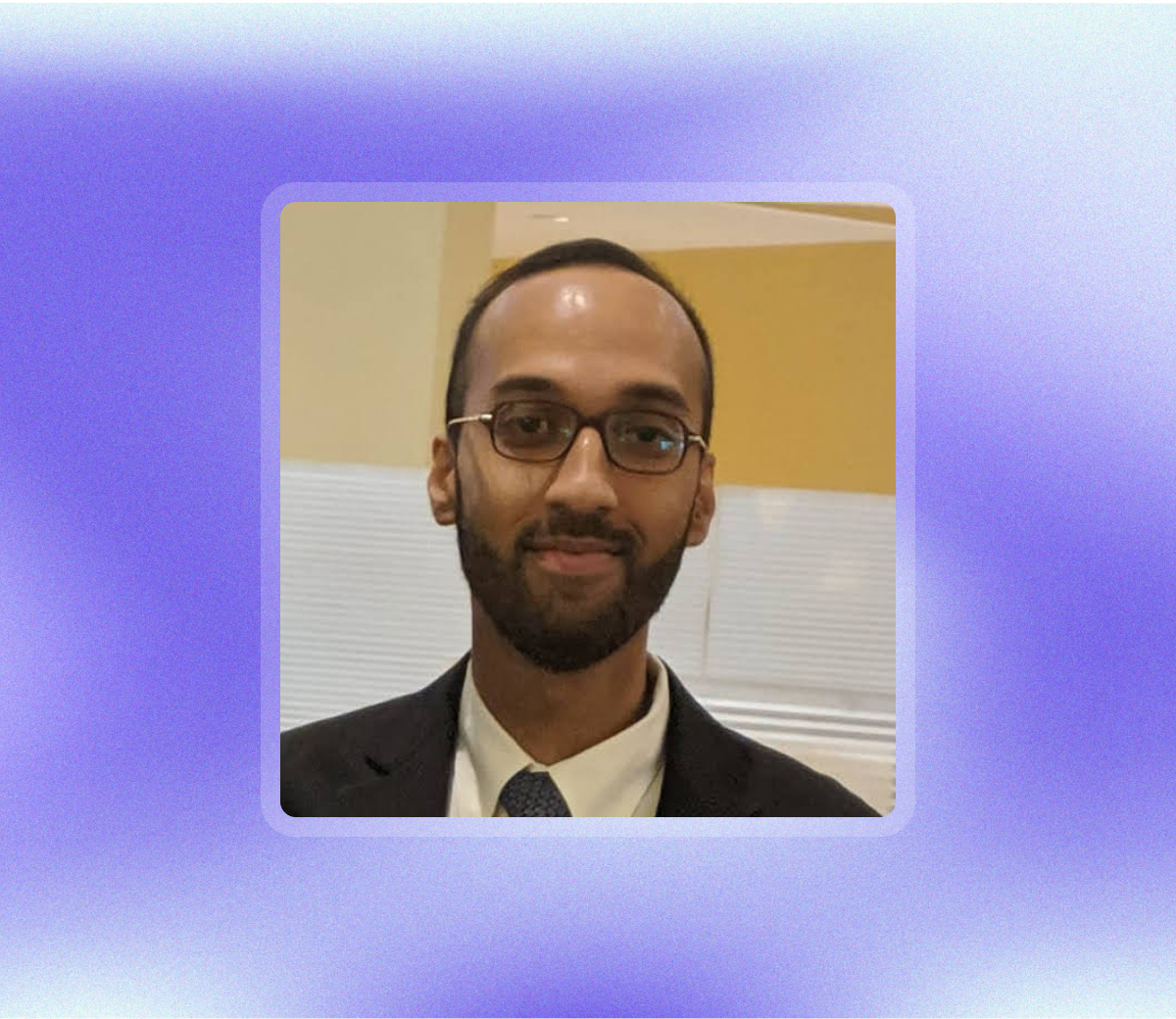 A man with glasses and a beard wearing a dark suit, white shirt, and tie stands in front of a beige indoor background, framed by a purple gradient border—embodying professionalism often associated with finance for physicians.